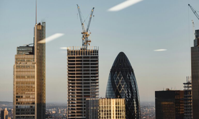 View of contemporary skyscrapers and cranes in London at sunset, featuring the iconic Gherkin building.