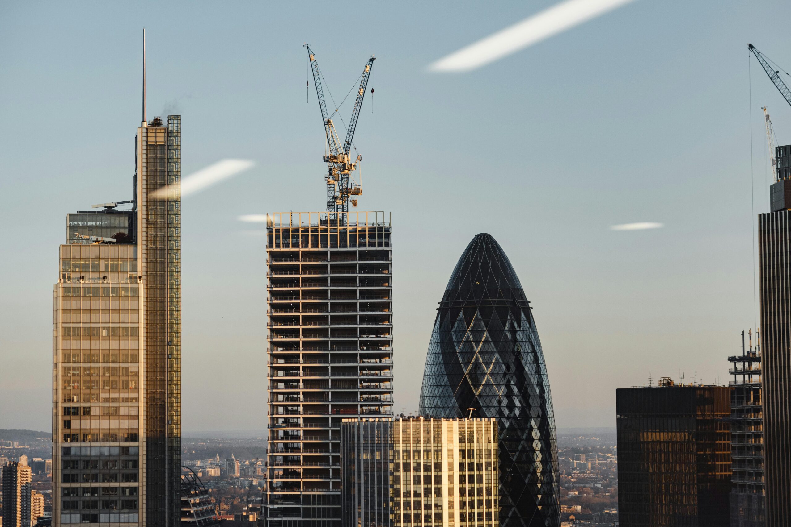 View of contemporary skyscrapers and cranes in London at sunset, featuring the iconic Gherkin building.