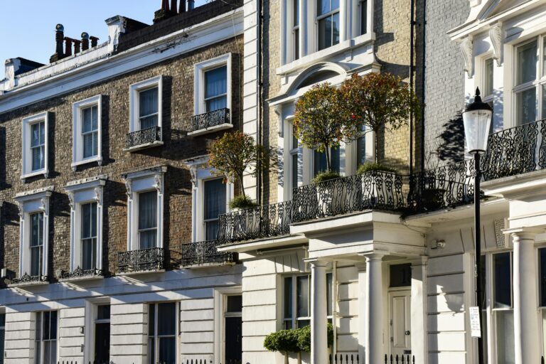 A row of classic London townhouses with detailed iron balconies under a clear blue sky.