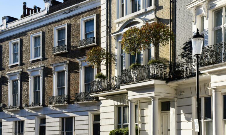 A row of classic London townhouses with detailed iron balconies under a clear blue sky.